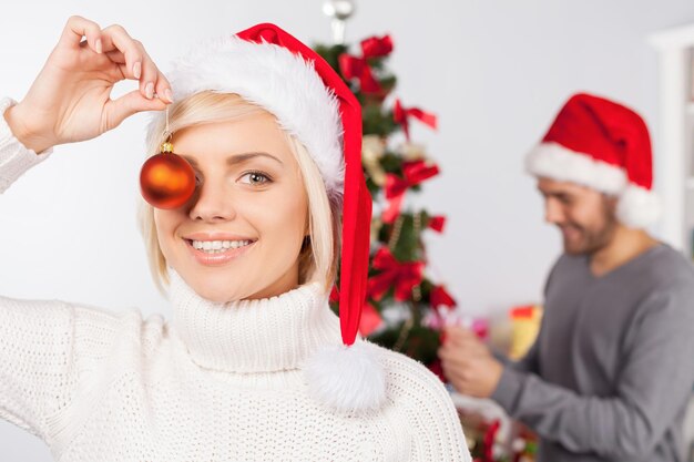 Kerst plezier. Speelse jonge vrouw die plezier heeft terwijl haar vriendje een kerstboom op de achtergrond versiert