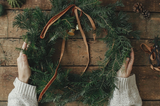 Kerst rustieke krans platte layVrouw handen met kerstkrans met lint en klokken op tafel