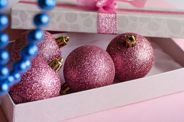 Kerst samenstelling. Geopende geschenkdoos met kerstballen op pastelroze. Detailopname. .