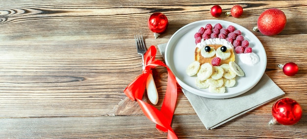 Kerst Santa Claus-gezichtsvormige pannenkoek met zoete verse frambozenbes en banaan op plaat houten achtergrond voor kinderen kinderen ontbijt diner. xmas food dessert nieuwjaarsdecoraties, rode ballen