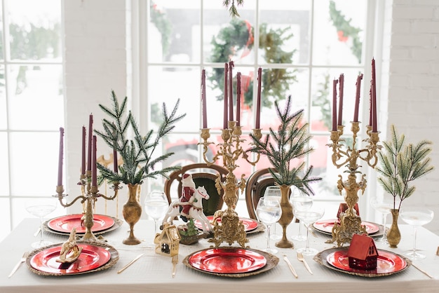 Kerst serveren van een feestelijk nieuwjaarsdiner Kaarsen in kandelaars vuren takken rode en gouden platen