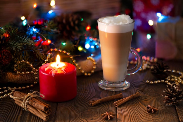 Kerst stilleven glas transparante hoge mok hete cappuccino kaneelstokjes rode kaars vakantie decor met dennentakken kegels kralen gezellige en milde winter avond achtergrond wintertijd