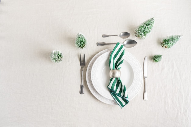 Kerst tabel instelling met witte borden, bestek, servet en met kerst decor op linnen tafellaken met kopie ruimte. Winter, feestelijke concept tafel die dient voor het nieuwe jaar.