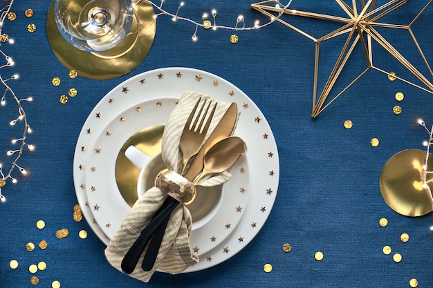 Kerst tafel opstelling met witte plaat en gouden gebruiksvoorwerpen en vergulde decoraties.