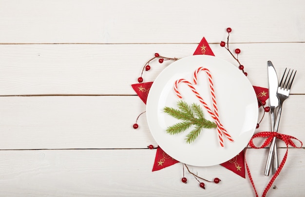 Kerst tafel setting met witte servies en rode versieringen op witte houten achtergrond. Bovenaanzicht. Ruimte kopiëren.