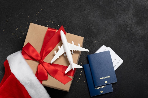 Kerst vliegtuig reizen concept. Paspoorten, speelgoed wit vliegtuig. Gouden sterren en Santa Cause-hoed op zwarte gestructureerde achtergrond. Geschenkdoos