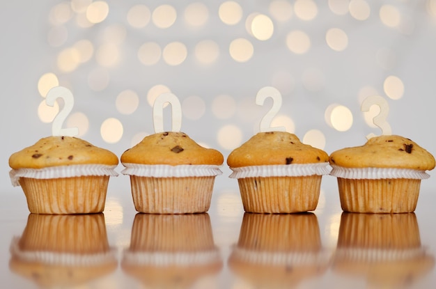 Kerst zoete cupcakes en kaarsen in de vorm van nummers 2023. Witte achtergrond met bokeh. Nieuwjaar