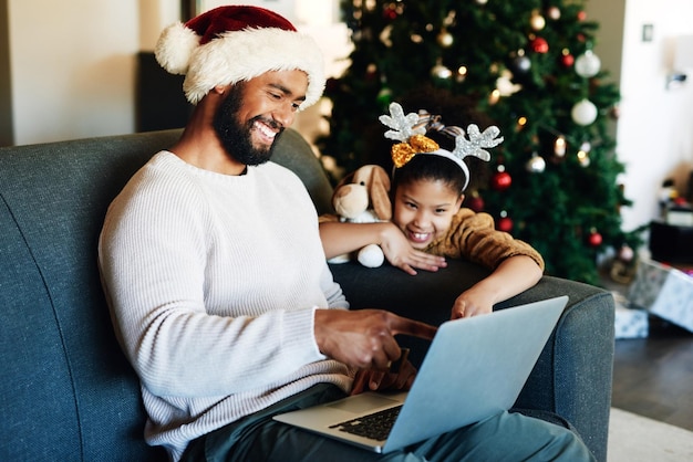 Kerst zwarte vader en dochter met laptop op bank op internet sociale media lezen en glimlachen Vakantie vader en meisje met pc gelukkig en hechting op bank in gezinswoning, woonkamer en web-app