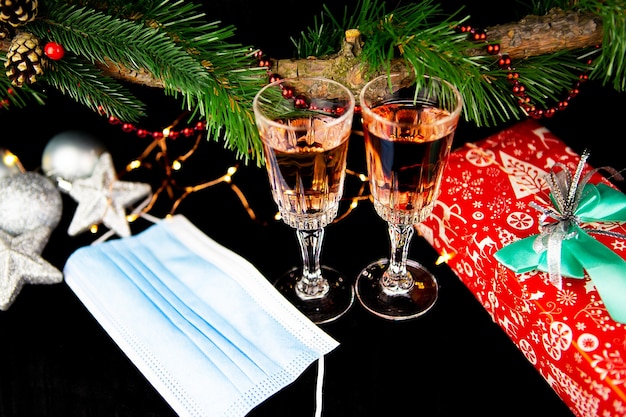 Kerstachtergrond met dennentakken, twee champagneglazen, cadeau, medisch masker, concept van nieuwjaarsdecor, close-up.