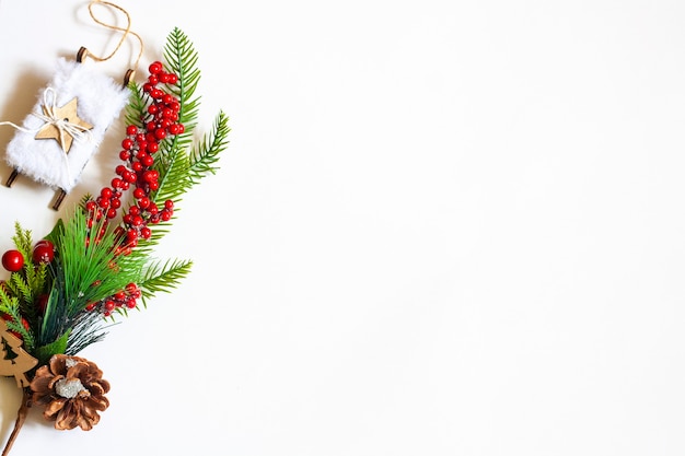 Kerstachtergrond, sparren takje met rode bessen en kerstspeelgoedslee op een witte achtergrond, kopieer ruimte