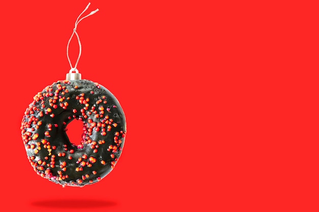 Kerstbal bal decoratie speelgoed gemaakt van zoete suiker chocolade zwart geglazuurde donut donut dessert op roze pastel achtergrond. Creatieve minimale vakantievoedselconcept kopieerruimte