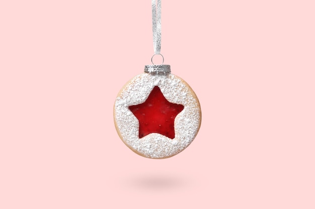 Kerstbal gemaakt van Linzer-koekjes die over een roze achtergrond hangen Minimal Christmas concept