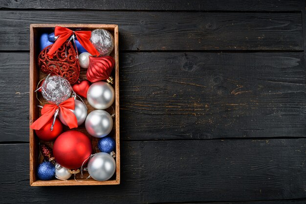 Kerstballen en speelgoed set, in houten kist, bovenaanzicht plat lag, op zwarte houten tafel achtergrond, met kopieerruimte voor tekst