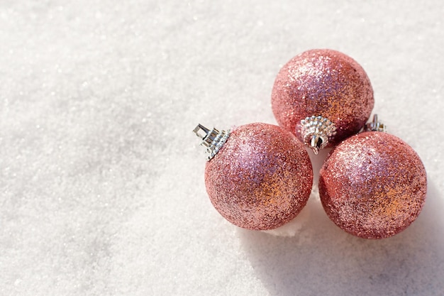 Kerstballen sneeuw. Roze glanzende kerstversieringen liggen op de sneeuw en schitteren.