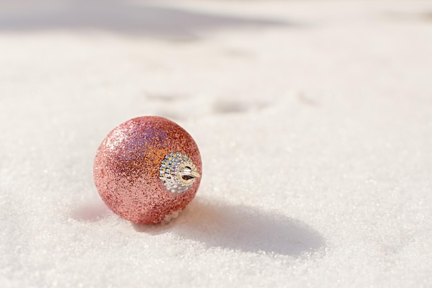 Kerstballen sneeuw. Roze glanzende kerstversieringen liggen op de sneeuw en schitteren.