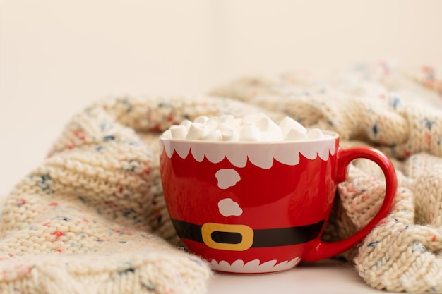 kerstbeker in de vorm van een kerstman met cacao en marshmallow staat naast een gebreide trui