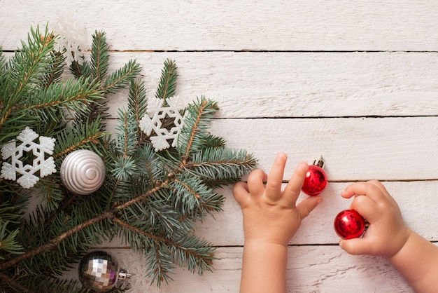 Foto kerstboom en baby handen op witte houten achtergrond. witte sneeuwvlokken. plat lag, bovenaanzicht. kopieer ruimte