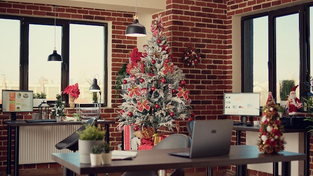 Kerstboom en versieringen in bedrijfskantoor, feestelijke ornamenten en lichten om kerstvakantie te vieren. lege werkplek met seizoensgebonden decor voor feest, kersttraditie.