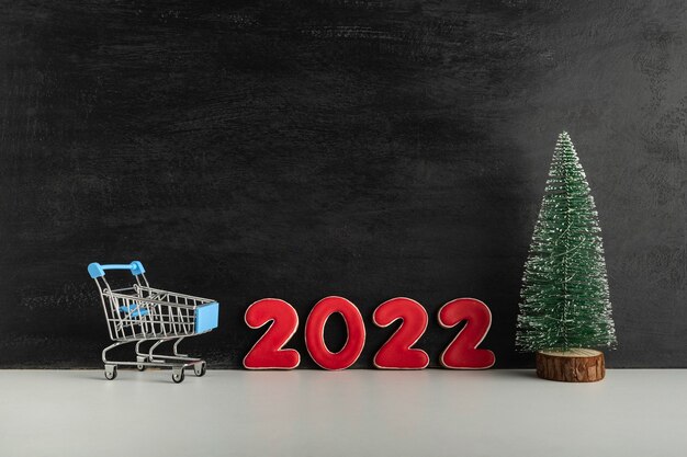 Foto kerstboom, karretje en nummers 2022 op donkere achtergrond. winkelen voor het nieuwe jaar. ruimte kopiëren