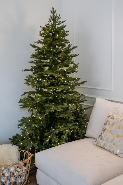 Kerstboom met cadeautjes en verlichting en bank in lichte en luchtige woonkamer