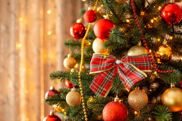 Kerstboom met grote strik en kerstballen op de voorgrond alles in rode en gouden kleuren