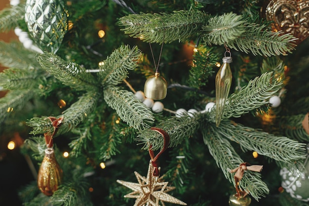 Kerstboom met vintage kerstballen en gouden lichten close-up Modern ingerichte kerstboomtakken met stijlvolle ornamenten in feestelijke kamer Wintervakantie voorbereiding sfeervolle tijd