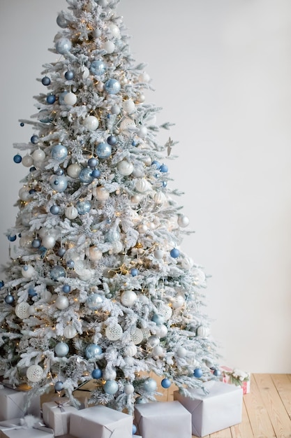 Kerstboom met zilveren en blauwe versieringen en lichtjes Gezellige kerstboom en geschenkdozen op een witte muurachtergrond