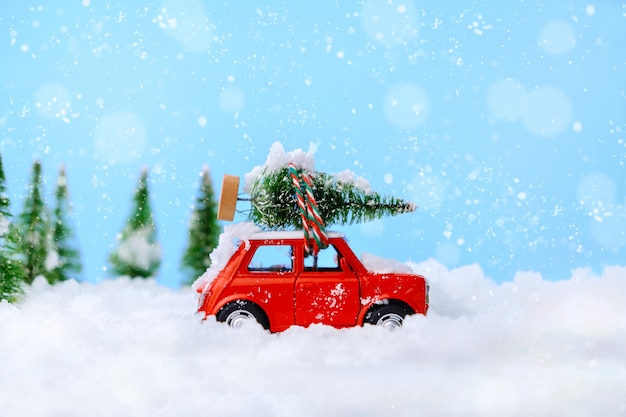 Kerstboom op rood autostuk speelgoed met vage boom en sneeuw. Viering kerstkaart