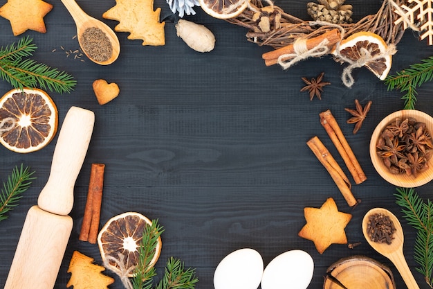 Kerstboom, peperkoekkoekjes, kruiden, bakbenodigdheden op zwarte houten ondergrond. Kerst, nieuwjaarswenskaart