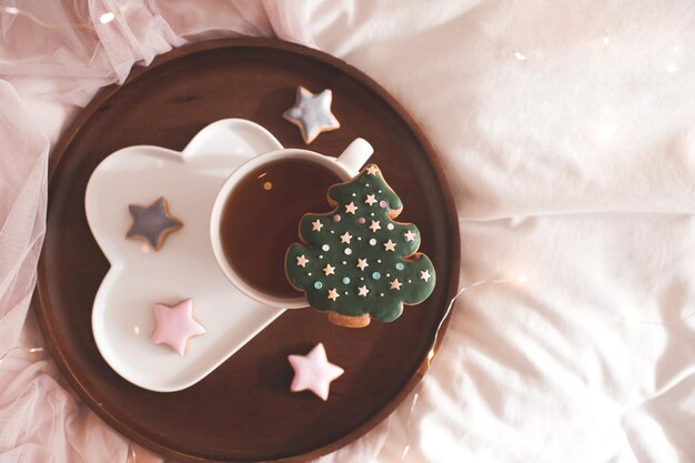 Kerstboompeperkoek op kopje thee op houten dienblad met gemberbroodsterren in bedclose-up. Bovenaanzicht. Winter vakantie seizoen.