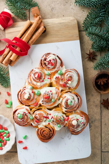 Kerstboomvorm kaneelbroodjes of kaneelbroodjes met kaneel en roomsaus op oude tegels achtergrond Feestelijk idee voor zelfgemaakte traditionele winter feestelijke dessertbroodjes gebak Bovenaanzicht