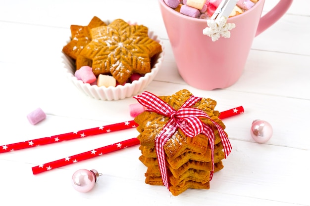 Kerstcacao met marshmallow in een roze kop en gemberkoekje op een houten tafel