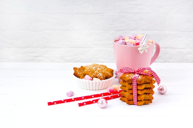 Kerstcacao met marshmallow in een roze kop en gemberkoekje op een houten tafel