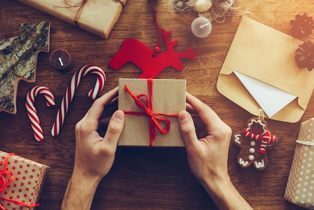 Kerstcadeau openen. Close-up bovenaanzicht van de man die de geschenkdoos opent op het houten bureau met kerstversieringen die rondslingeren