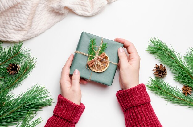 Kerstcadeaudoos in vrouwelijke handen over witte achtergrond met pijnboomtakken