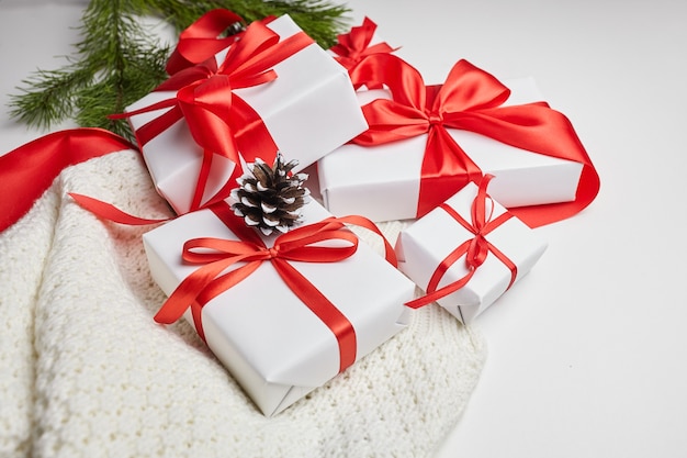 Kerstcadeaudozen met rood lint en gebreide trui met groene dennenboomtak en kegels op wit