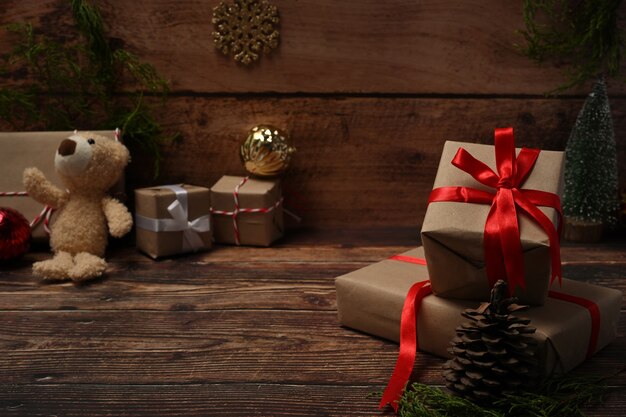 Kerstcadeaudozen met rood lint, teddybeer, dennenappels en dennentakken op houten tafel.