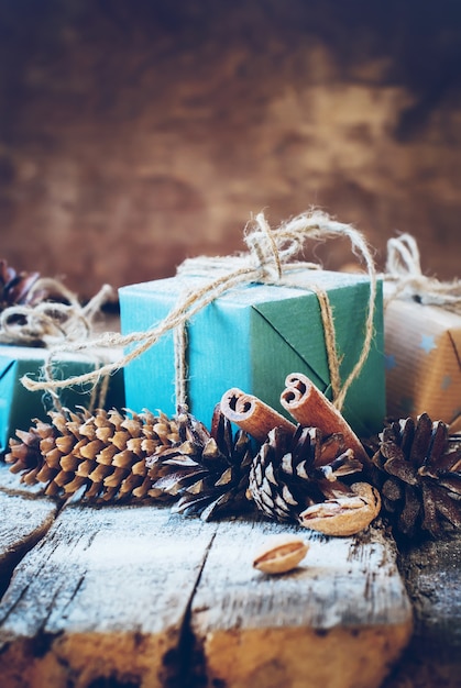Kerstcadeaus met linnen koord, kaneel, dennenappels, noten op houten achtergrond