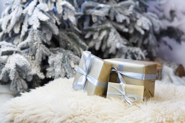 Kerstcadeaus versierd met zilveren satijnen lint strikken op zacht pluizig tapijt op wazig besneeuwde dennenboom achtergrond, close-up, selectieve focus. Winter vakantie concept