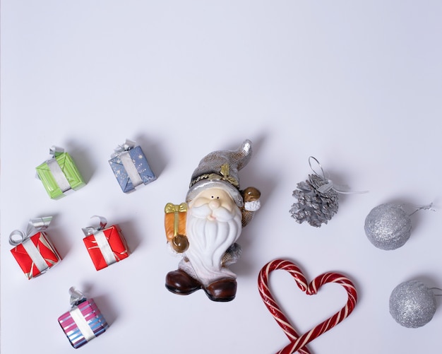 Kerstcompositie met de kerstman of kabouter, geschenken, kerstsnoepstokken in de vorm van een hart, paarse en zilveren ballen, dennenappels op een witte achtergrond, plat leggen, bovenaanzicht, kopieerruimte