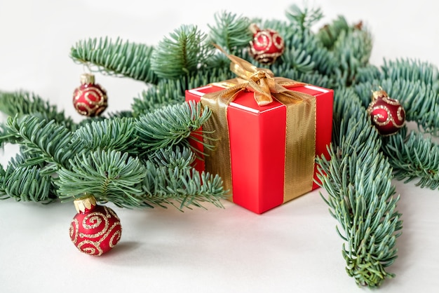 Kerstcompositie met rode geschenkdoos en dennentakken versierd met glanzende ballen