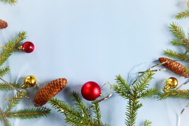 Kerstcompositie rode en gouden kerstballen met dennentakken op een pastelblauw oppervlak.