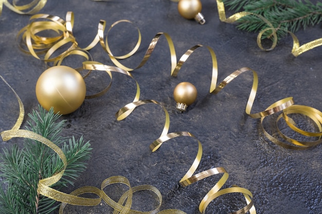 Kerstcompositie van gele kerstballen, dennentakken en een gouden lint op een zwart met gouden reliëfachtergrond.