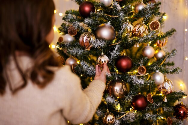 Kerstconcept - achteraanzicht van een klein meisje dat de kerstboom versiert met kerstballen en lichtjes