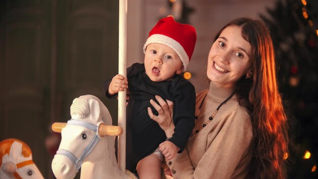 Kerstconcept een jonge moeder met haar baby die in de camera kijkt baby zit op de carrousel