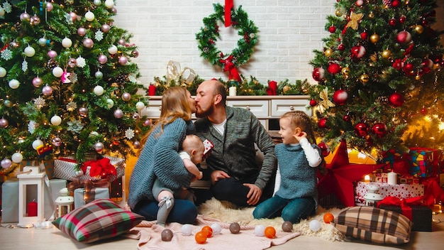 Kerstconcept gelukkige familie zit in de kerstomgeving en wisselt geschenken uit, mama en papa zoenen