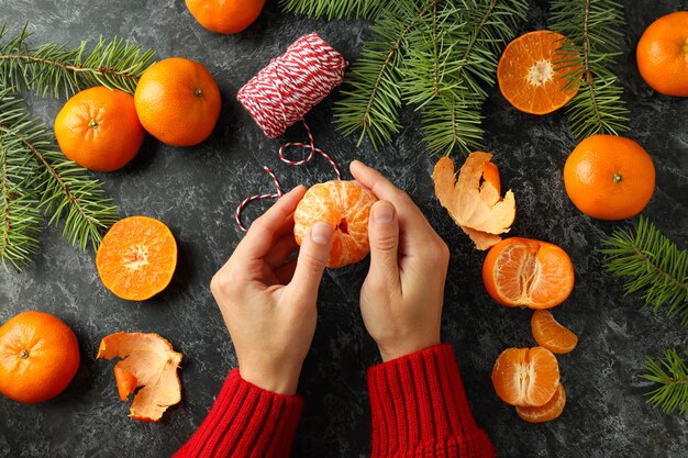 Kerstconcept met vrouwelijke handen houdt mandarijnen vast op zwarte rokerige tafel