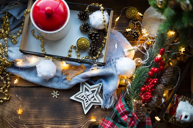 Kerstdecor bij het raam op een gezellige houten vensterbank met een mok met een drankje en een koektrommel. Kerstverlichting, kerstboomtak, ontbijtblad stilleven