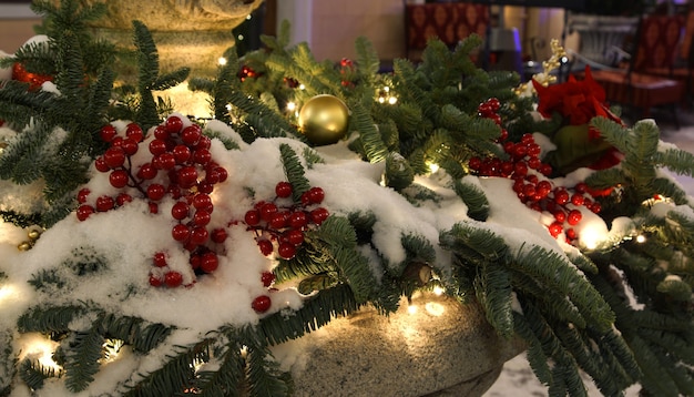 Kerstdecoratie met rode bessen en dennentakken en slingers bedekt met sneeuw buiten in de winter.