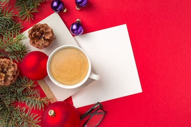 Kerstdecoraties met Kladblok, pen, glazen en kopje koffie op rode werkruimte bovenaanzicht